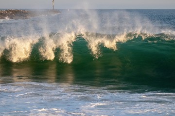 Large blue green wave crashing in the ocean during sunset