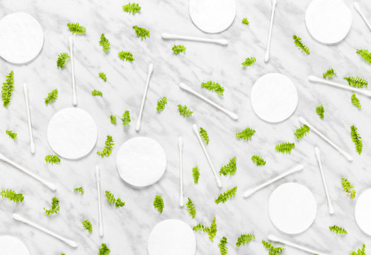Cotton pads, swabs and green leaves on marble background