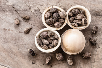 Spilled whole black cardamom in coconut bowls on wooden background