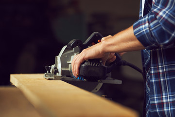 The carpenter using circular saw for cutting a wooden plank in his workshop