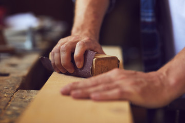 Close-up of carpenter using sandpaper on a wooden plank in a carpentry shop - obrazy, fototapety, plakaty