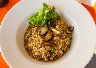 Delicious risotto with mushrooms and lettuce on white plate from top. Tasty vegetarian dish