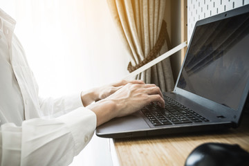 Working at home with notebook computer, Man hands on keyboard writing work in the morning background.