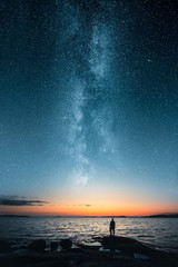 Silhouette of a man looking up on stars of the milky way with last light of sunset glows on the horizon - 212940791