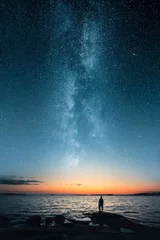 Fototapeten Die Silhouette eines Mannes, der mit dem letzten Licht des Sonnenuntergangs auf die Sterne der Milchstraße blickt, leuchtet am Horizont © Jamo Images