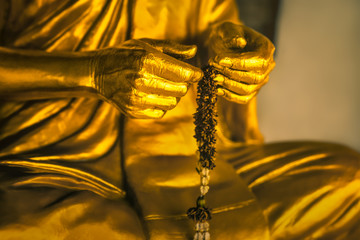 golden statue of a buddhist monk - close-up of praying hands with prayer beads