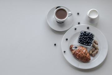 Breakfast from coffee, milk, croissants and blueberries. White background. White dishes.