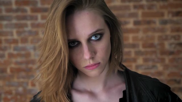 Young sexy strong girl with smoky eyes is staring at camera, brick background