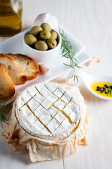 Baked camembert cheese. Fresh Brie cheese and a slice on a wooden board with nuts, honey, rosemary, baguette bread grilled toasts and leaves. Brie type of cheese. Italian, French cheese.