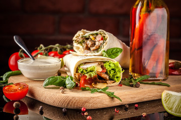 Mexican cuisine, burrito with chicken, cherry tomatoes, lettuce, mushrooms, rucola and chili peppers, on a black background. With salsa sauce. Copy space, selective focus