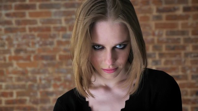Young sexy girl with smoky eyes is watching at camera, flirt concept, brick background