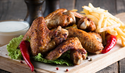 Close-up photo of bbq chicken wings with fries and beer. Barbeques meat with sauces, ketchup, mayonnaise. Fast and junk food concept. 
