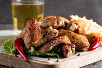 Close-up photo of bbq chicken wings with fries and beer. Barbeques meat with sauces, ketchup, mayonnaise. Fast and junk food concept. 