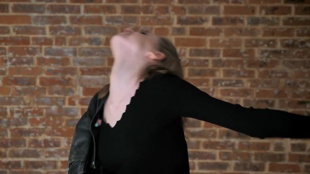 Young sexy girl with smoky eyes is dancing, shaking head, rock music, brick background, side view