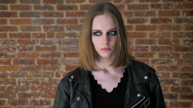 Young sexy alienated girl with smoky eyes is watching at camera, sadness, brick background