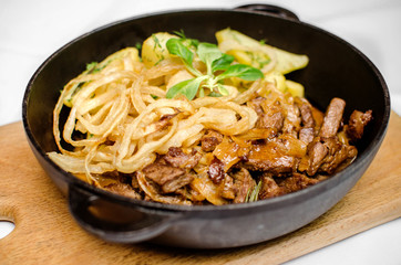 Lunch from roasted meat of varnish and potatoes in a black frying pan on a wooden kitchen board