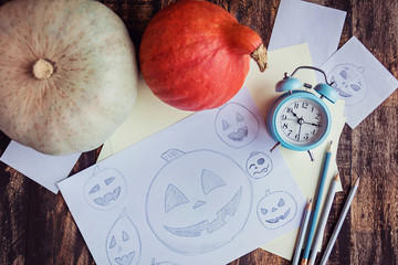 Pumpkings, pencil sketches and alarm clock on brown wooden table. Preparation to halloween holiday.