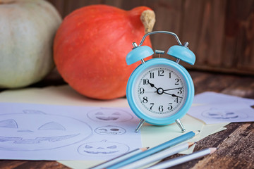 Pumpkings, pencil sketches and alarm clock on brown wooden table. Preparation to halloween holiday.