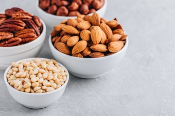 Pine nuts, almonds, pecans and hazelnuts in white bowls on grey background. Mixed nuts. Healthy food and snack.