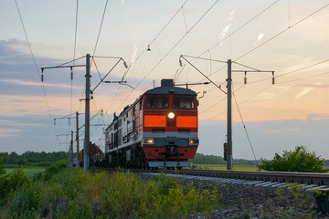locomotive with a freight train rides in the evening through the field
