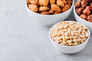 Pine nuts, almonds and hazelnuts in white bowls on grey background. Mixed nuts. Healthy food and snack.