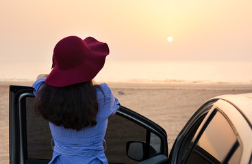 Girl facing beach sunset by the car