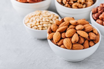 Almonds, pecans, walnuts, pine nuts and hazelnuts in white bowls on grey background. Assortment of nuts.