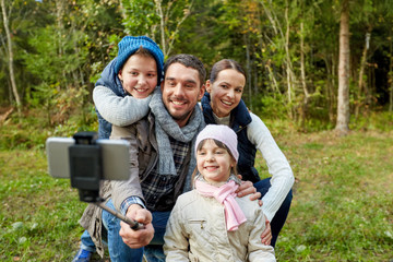 family and technology concept - happy mother, father, son and daughter taking picture by smartphone on selfie stick outdoors