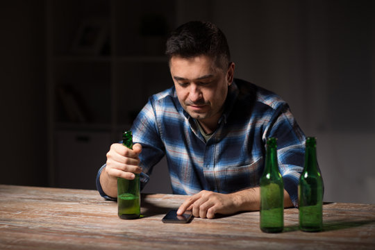 alcoholism, alcohol addiction and people concept - drunk man with smartphone and bottle of beer at night