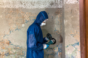 Worker in blue protective suit, glasses and respirator holding an angle grinder