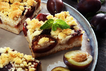 Fototapeta na wymiar Rustic plum cake on wooden background with plums around.
