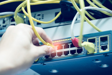 Administrator hand connecting network cables in server cabinet to switches.