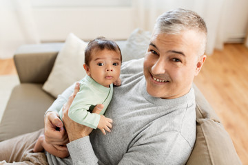 family, fatherhood and people concept - happy father with little baby boy sitting on sofa at home