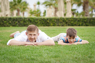 Naklejka na ściany i meble Father and son are laying at the lawn at the hotel. they are having a rest and looking to the camera.