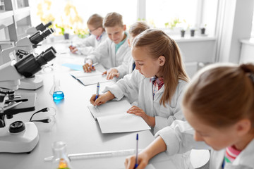 Fototapeta premium education, science and children concept - kids studying chemistry at school laboratory and writing to workbooks