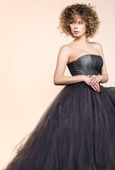 Fototapeta na wymiar Fashion image of a beautiful young woman in a dark gray dress. Golden curly hair and light makeup