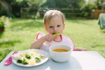 Portrait of adorable baby girl eating puree sitting at baby table outdoor