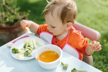 Portrait of adorable baby girl eating puree sitting at baby table outdoor