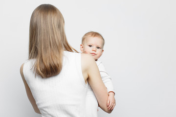 Young mother holding baby girl standing over white background.