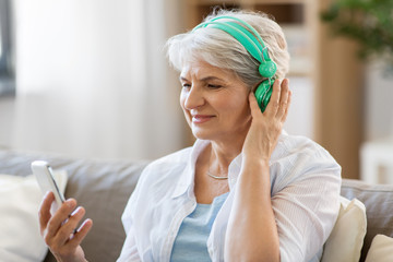 technology, people and lifestyle concept - happy senior woman in headphones and smartphone listening to music at home