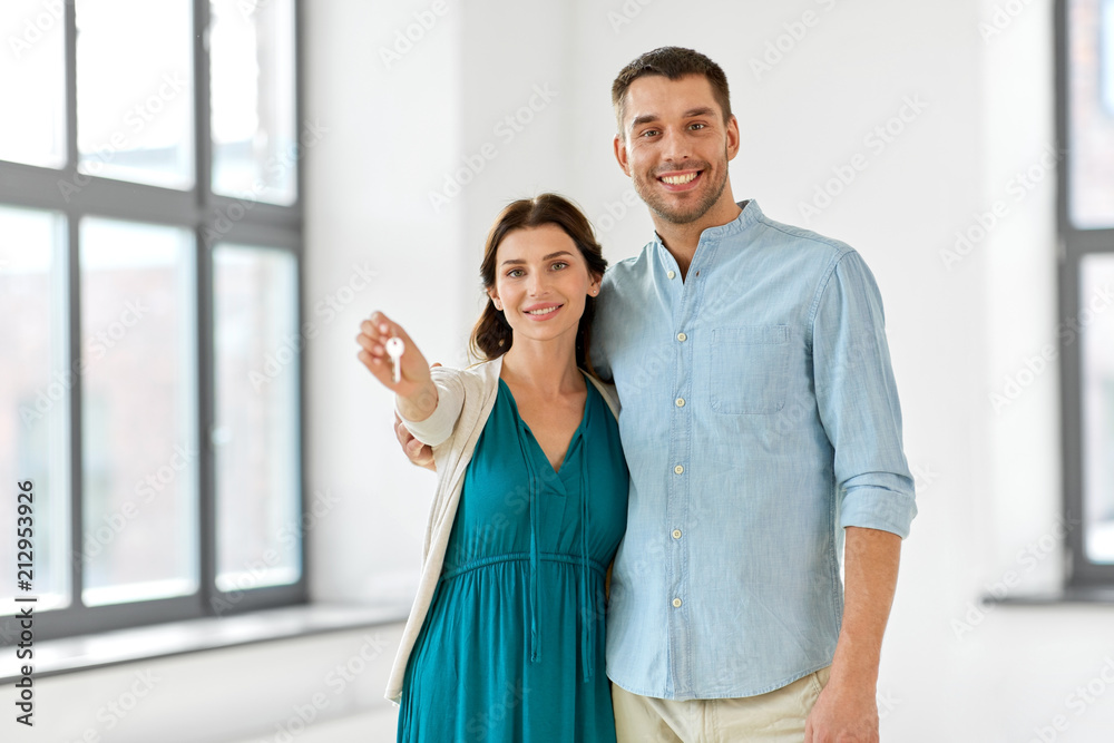 Sticker mortgage, people and real estate concept - happy couple with keys at empty room of new home