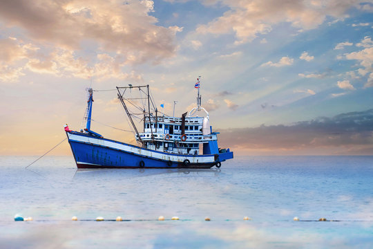 Fototapeta Blue - White Fishing Boat In The Sea And Dramatic Clouds At Sunrise.