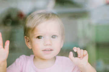 Portrait of cute baby girl behind glass, closeup