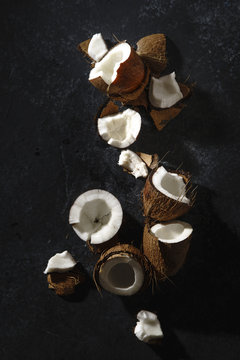 Cracked coconut arranged on dark textured background. Hard light.