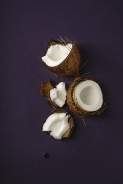 Cracked coconut arranged on dark purple background
