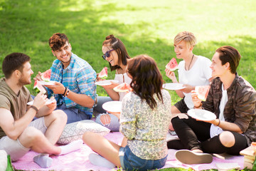 friendship, leisure and summer concept - group of happy friends eating watermelon at picnic in park
