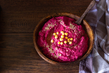 Roasted beet hummus in bowl with chickpea, sesame seeds and healthy chips over wooden surface. Snacks concept