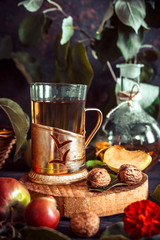 Apple tea in a glass goblet and a decanter and a basket with ripe apples on a wooden table in vintage style