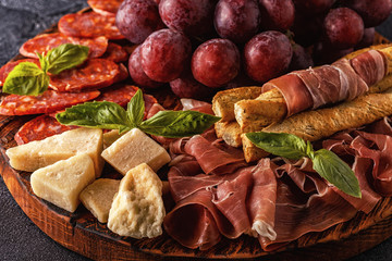 Prosciutto, sausage, wine, grape, parmesan on dark table.