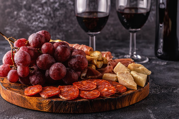 Prosciutto, sausage, wine, grape, parmesan on dark table.